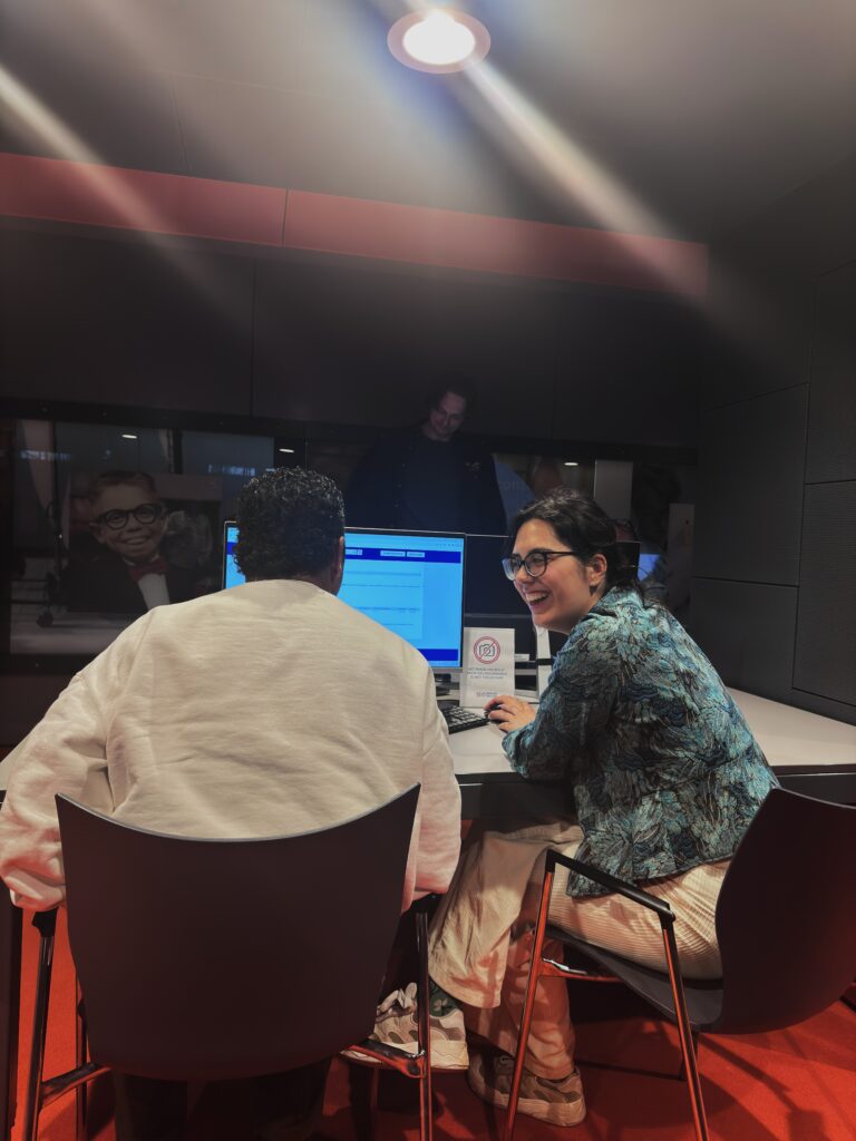 Beschrijving (voor context / publicatie):Tijdens een co-creatiesessie van Sounds Familiar bij Beeld & Geluid werken deelnemers samen achter een computer aan het doorzoeken en duiden van audiovisueel archiefmateriaal. In een informele setting wordt kennis gedeeld, gelachen en actief gezocht naar nieuwe perspectieven binnen bestaande beelden. Alt-tekst (toegankelijkheid): Twee deelnemers zitten naast elkaar achter een computer bij Beeld & Geluid en bekijken archiefmateriaal tijdens een sessie van Sounds Familiar.